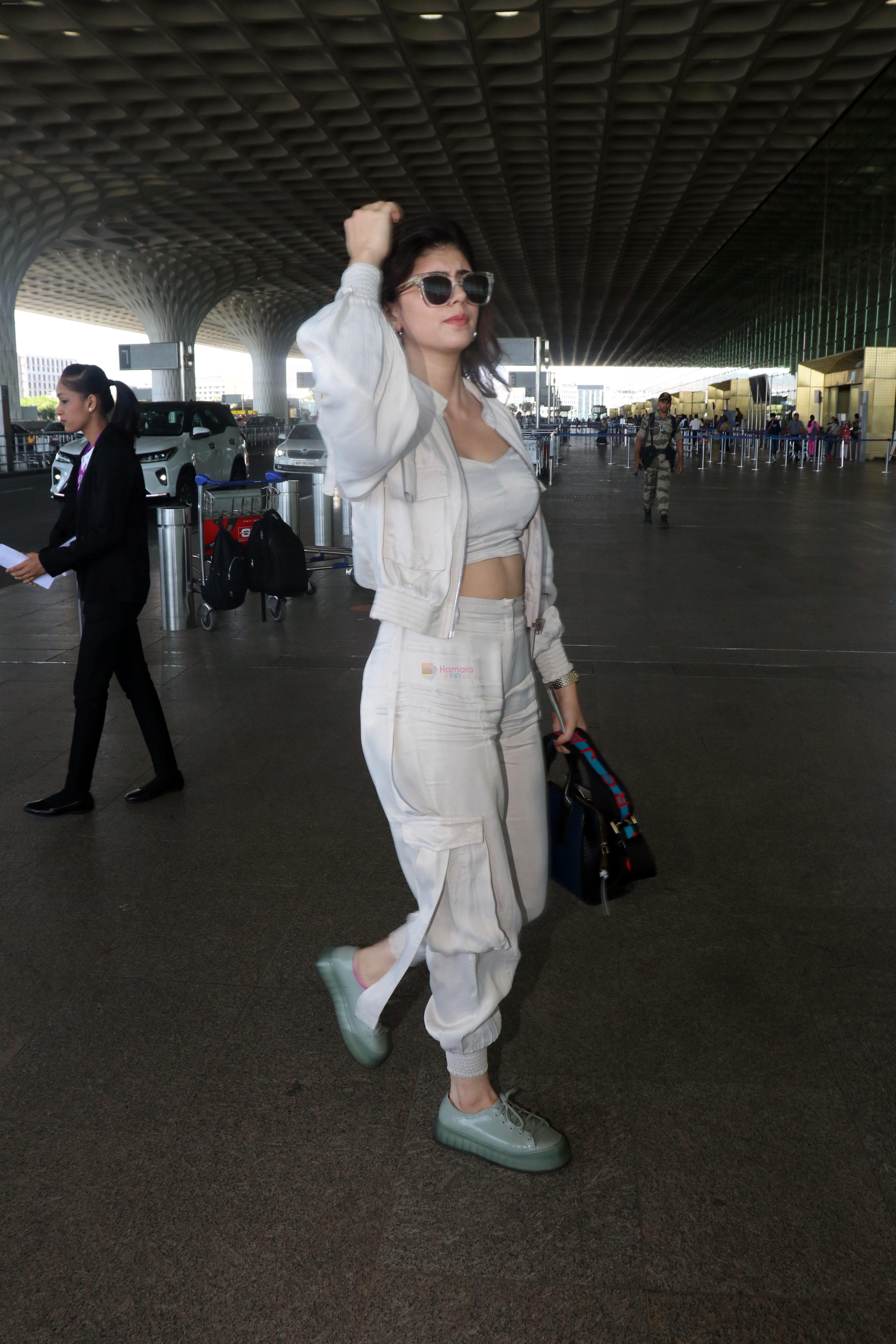 Sanjana Sanghi holding bag wearing cream colored long sleeved top and trousers and grey footwear with laces