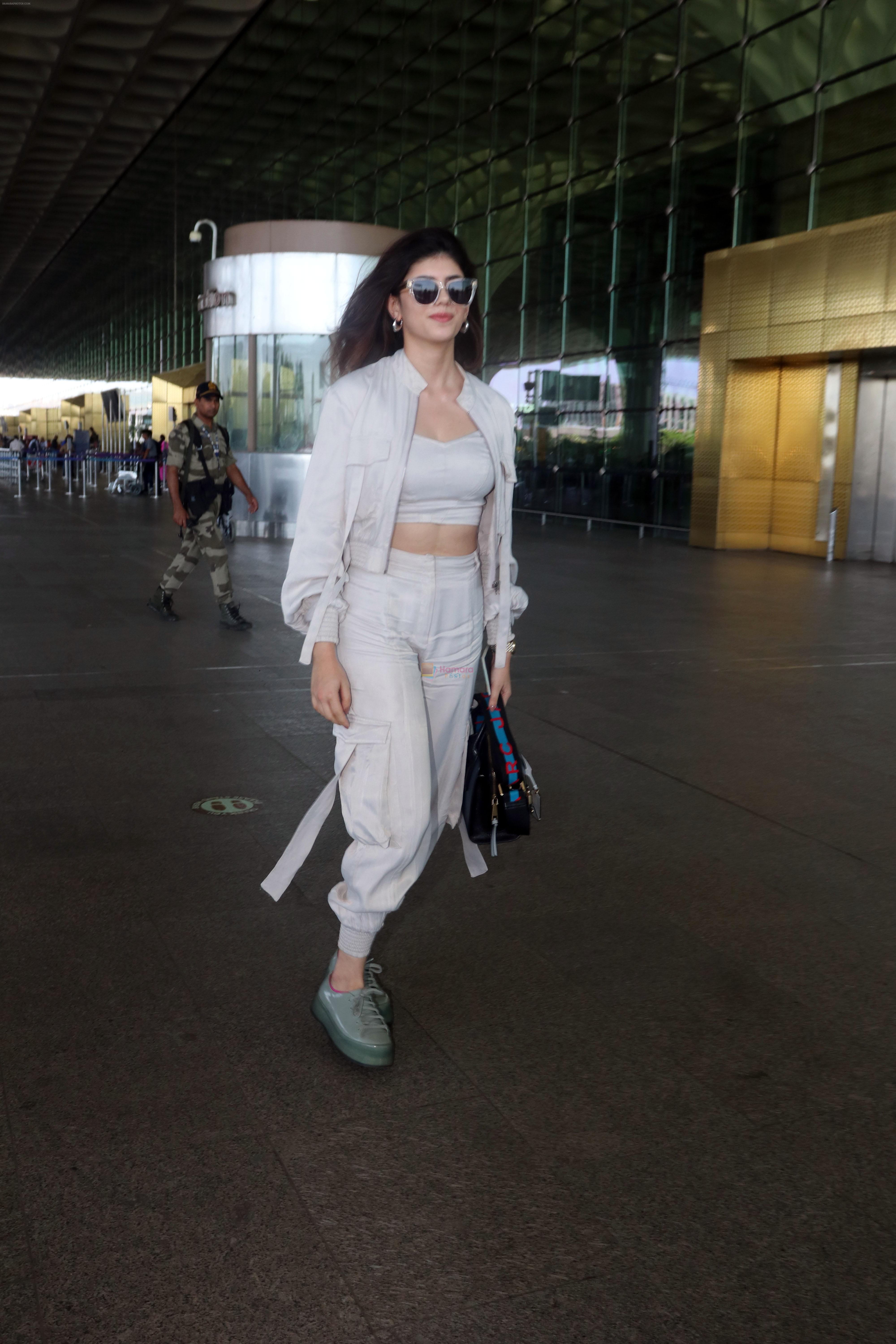 Sanjana Sanghi holding bag wearing cream colored long sleeved top and trousers and grey footwear with laces
