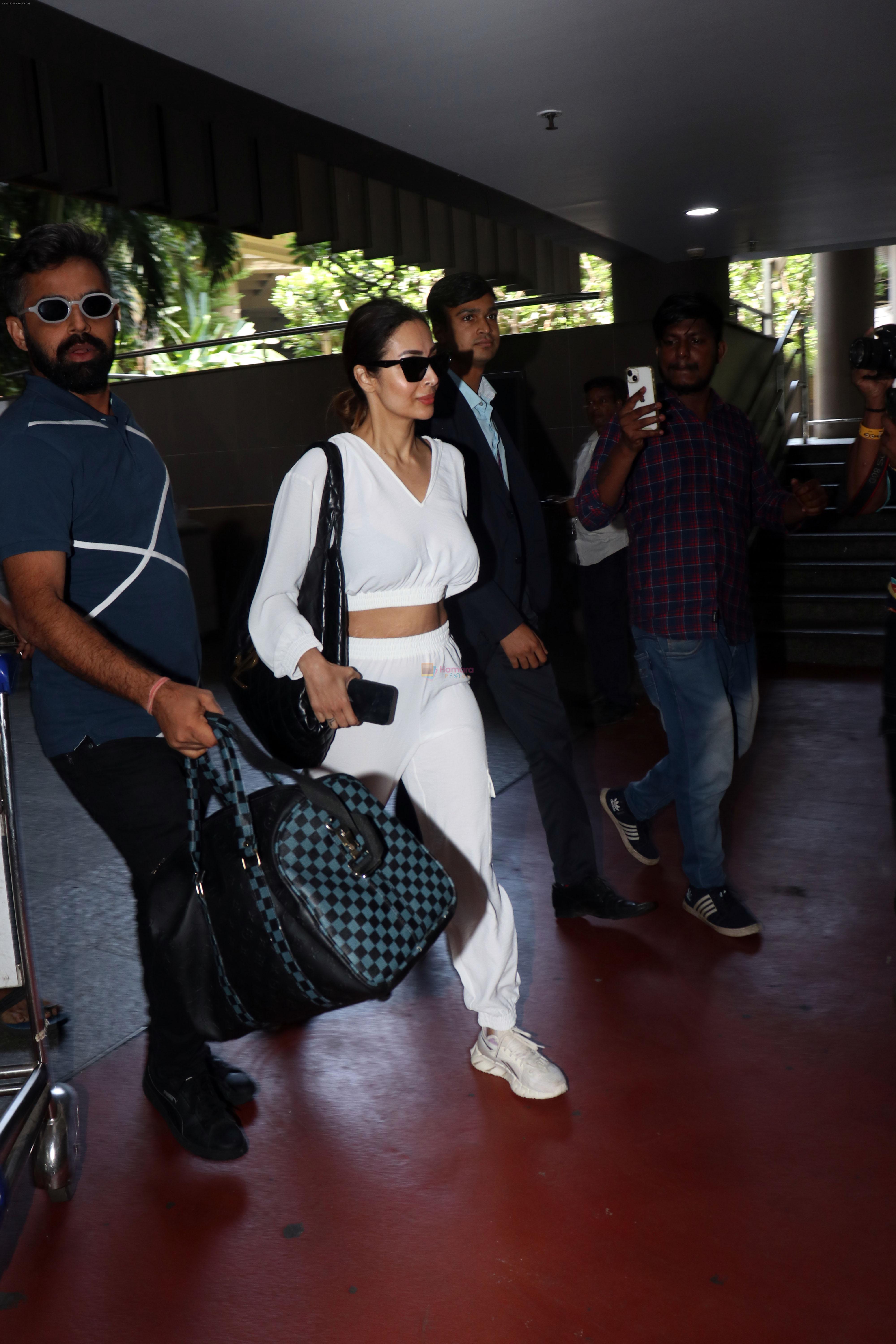 Malaika Arora in white wearing dark glasses white sneakers and holding black Chanel Bag