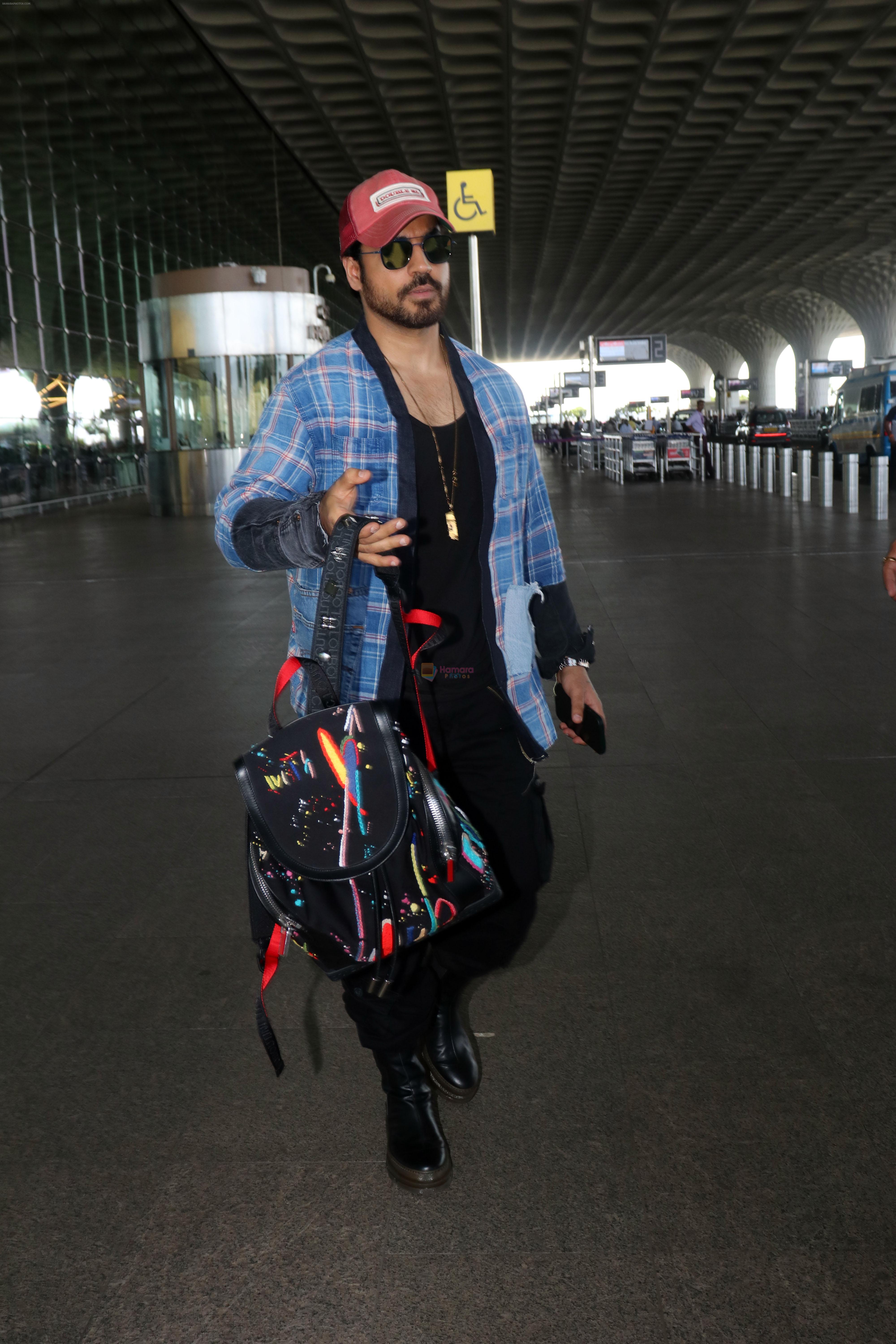 Gautam Gulati holding Christian Louboutin Explorafunk Backkpack dressed in Black with a red cap and blue jacket